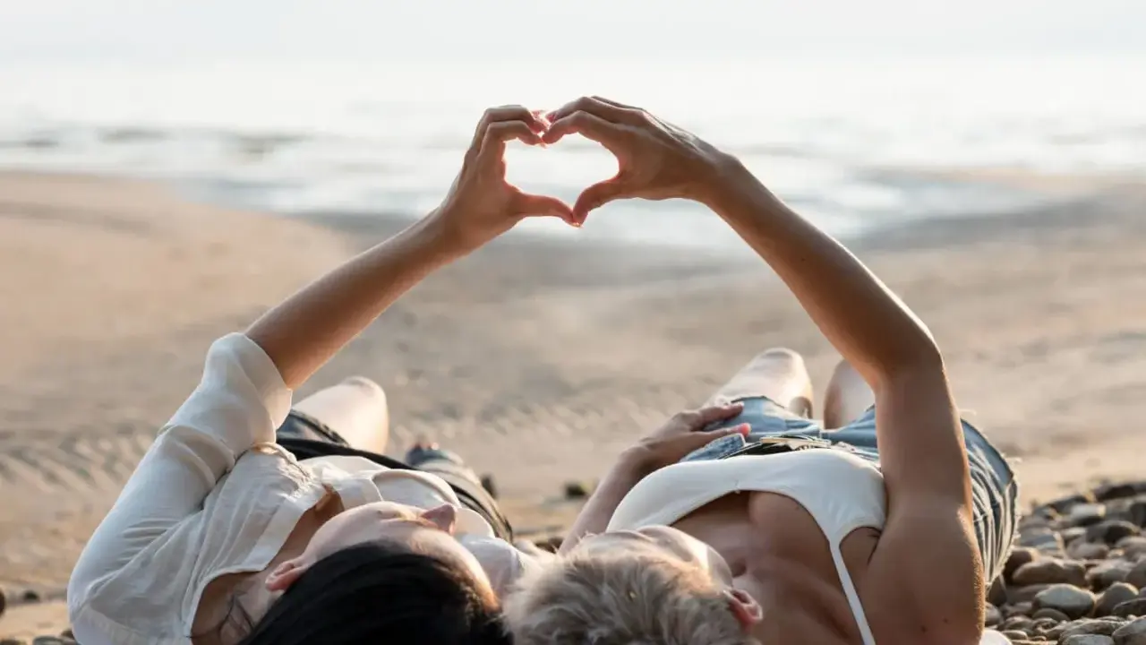 Para, które właśnie wzięło ślub, leży na plaży, tworząc serce dłońmi. Idealne miejsce na podróż poślubną.