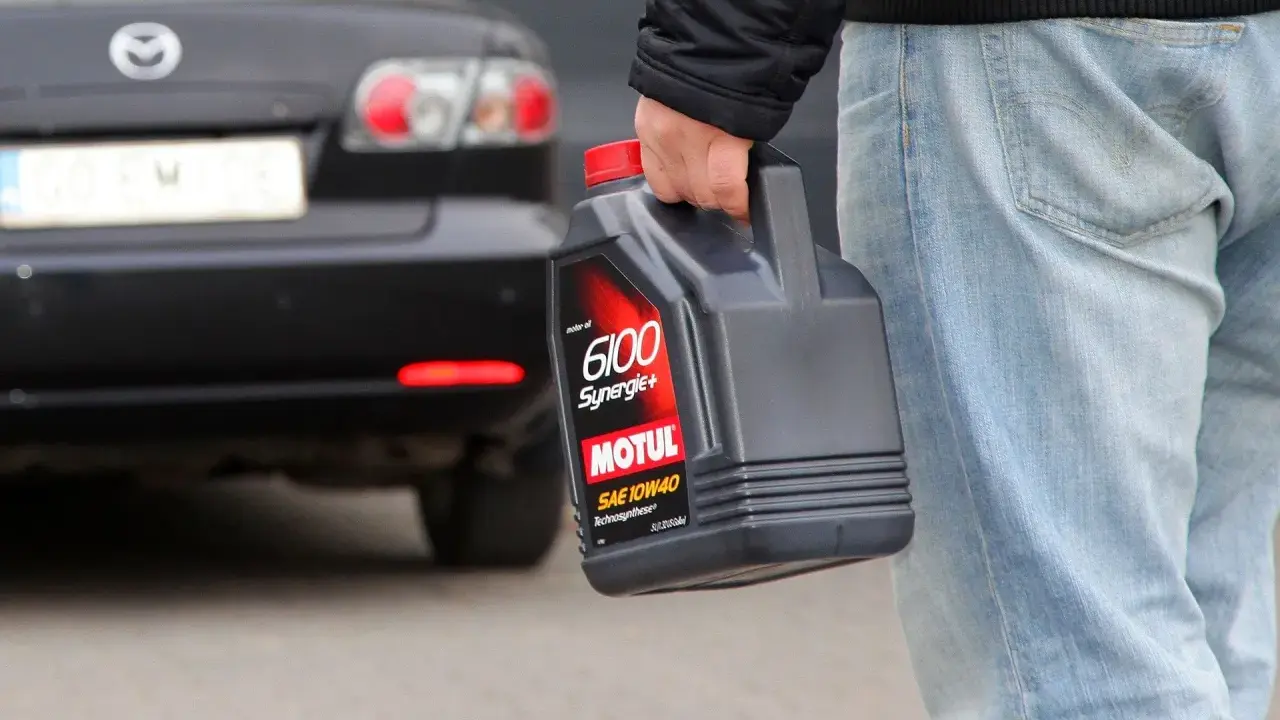 Mężczyzna niesie kanister z olejem silnikowym Motul, gotowy do recyklingu.