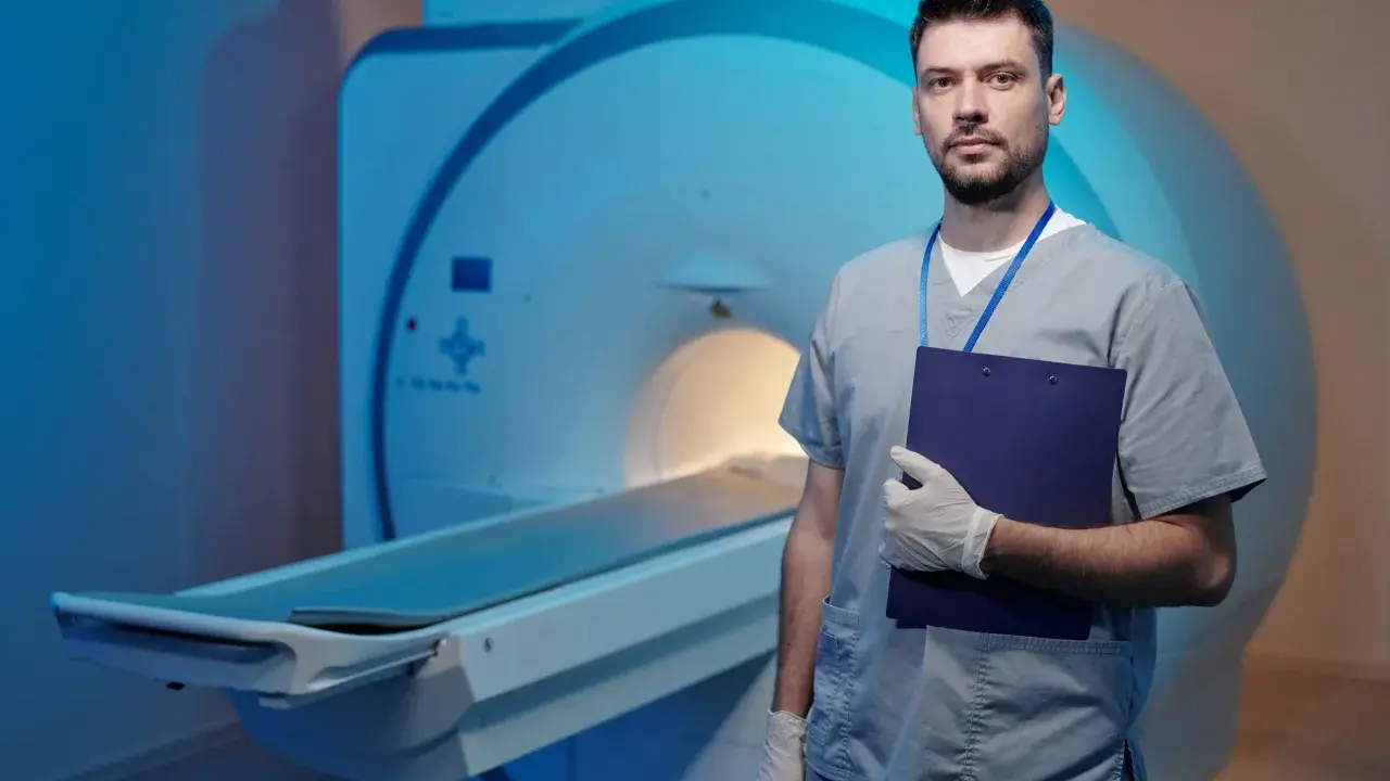 Lekarz w rękawiczkach z teczką stoi obok aparatu MRI. Dyskutuje o powikłaniach po rezonansie magnetycznym bez kontrastu.