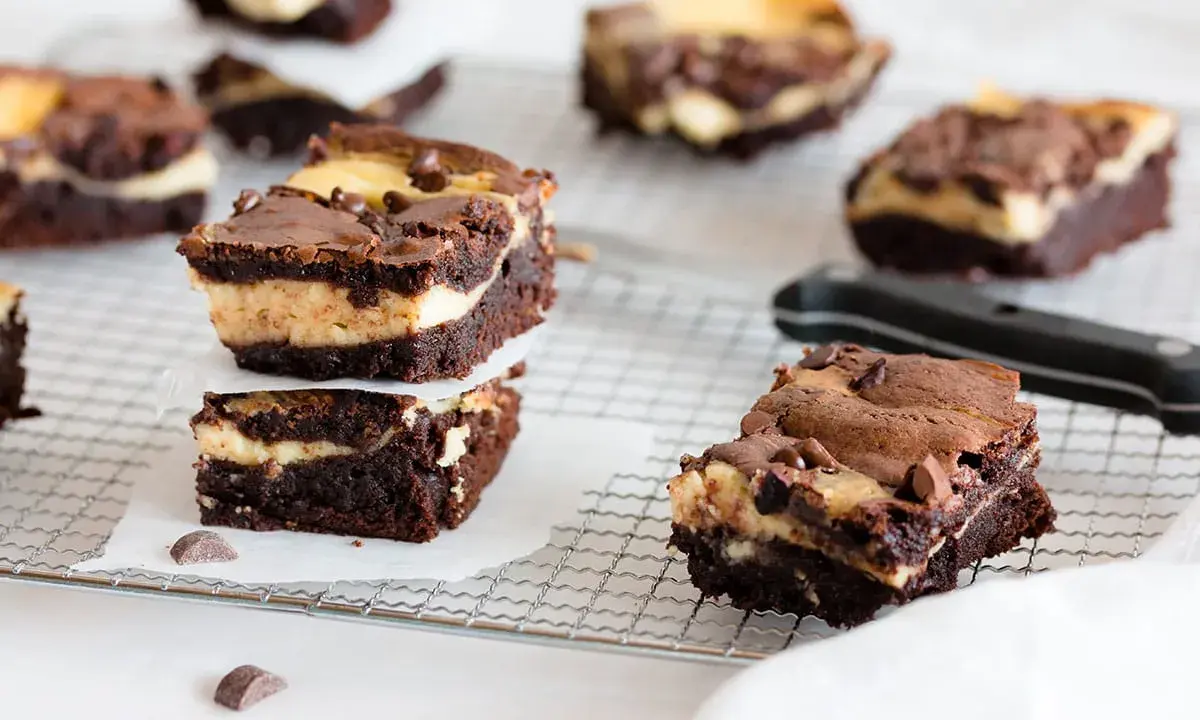 Schokoladige cheesecake brownies mit cremiger Füllung und Schokostückchen, gestapelt auf einem Gitter.