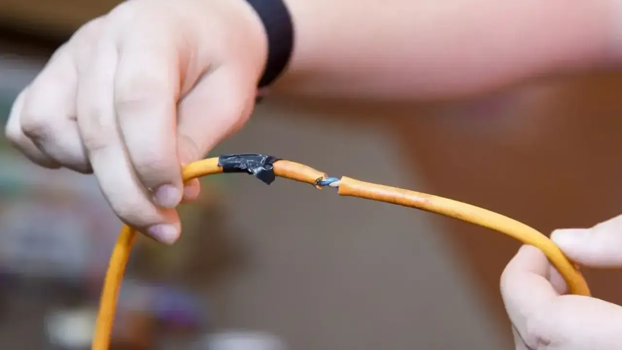 Ręce trzymające pomarańczowy kabel, który jest uszkodzony. Pokazuje, jak połączyć kable bez lutowania, używając taśmy izolacyjnej.