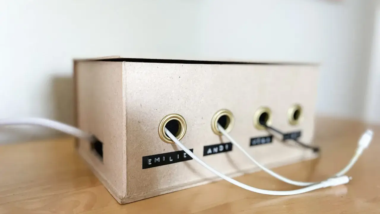 Kreative ladekabel aufbewahrung selber machen aus einem Karton. Kabel sind ordentlich durch Ösen geführt und beschriftet.