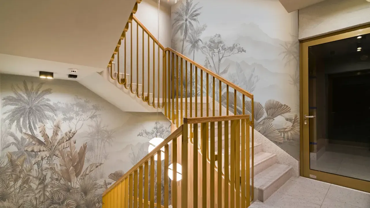 Habillage mur cage d'escalier avec un décor tropical en camaïeu. Escalier en marbre et rambarde en bois doré.