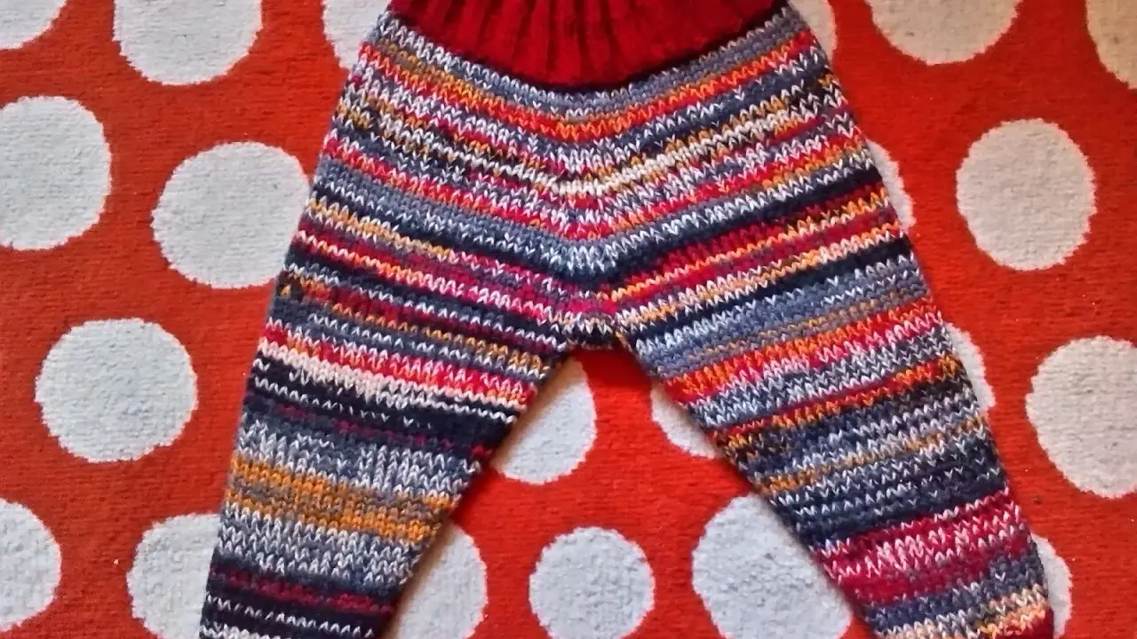 Pantalón de punto para bebé con rayas multicolores y cintura roja, sobre fondo de lunares.