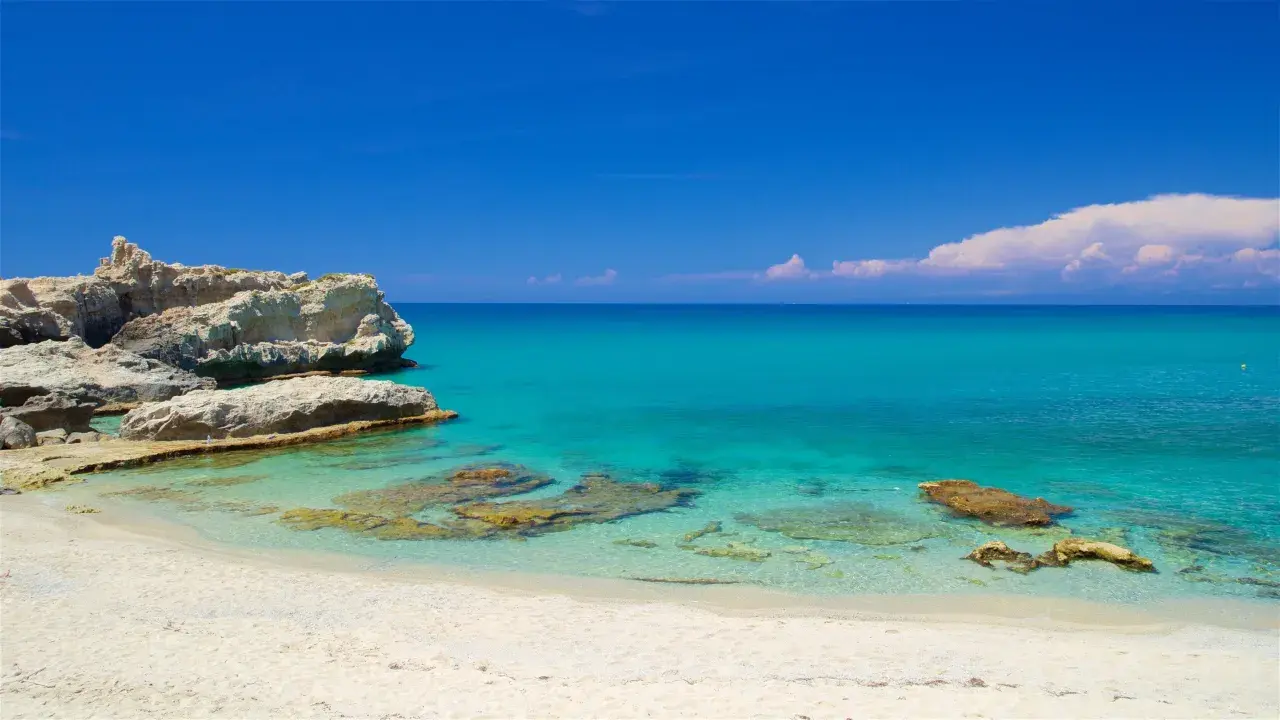 Spiaggia di Santa Domenica con rocce bianche e mare cristallino sotto un cielo azzurro.