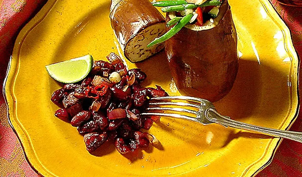 En hel aubergine i ugn, fylld med grönsaker, serveras med en röra av bönor och chili på en gul tallrik.
