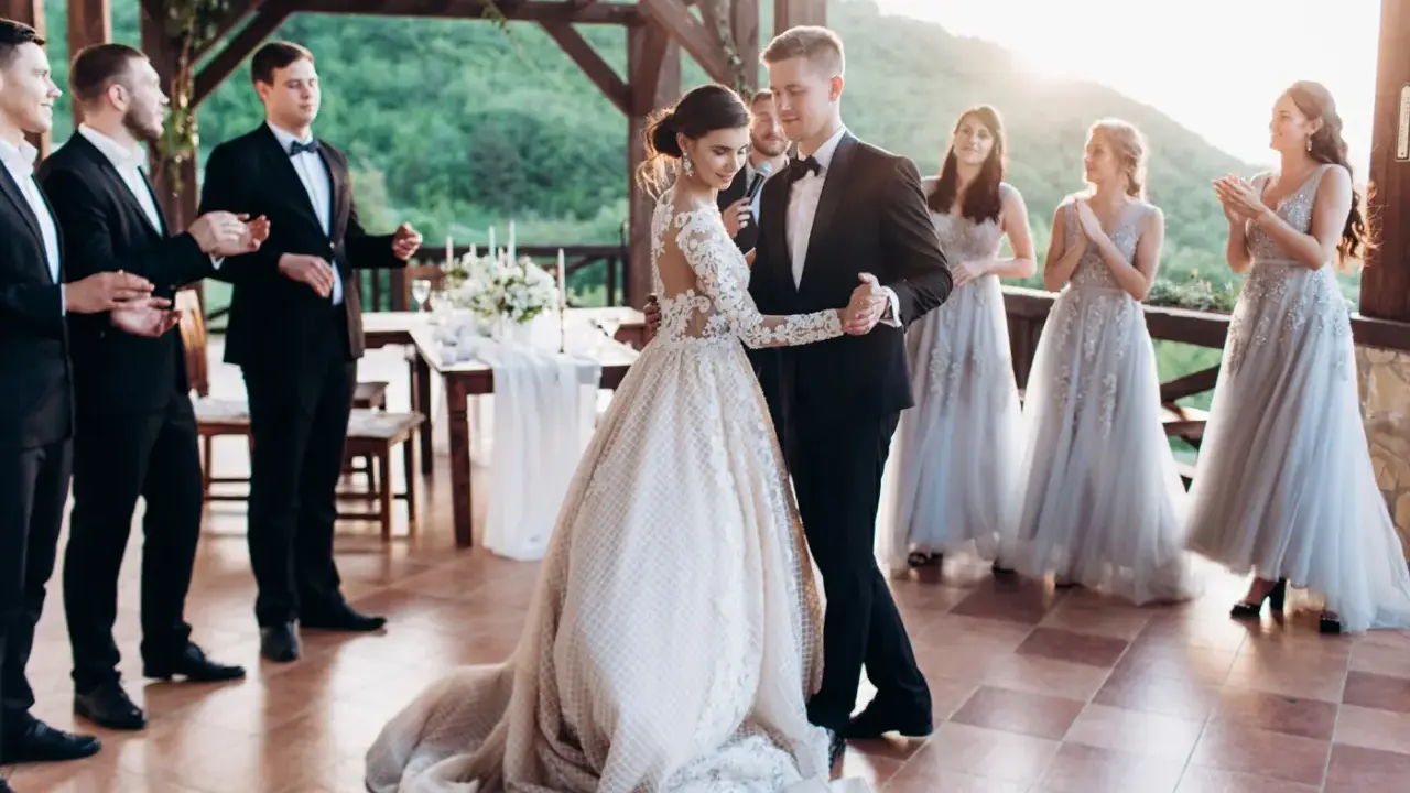 Para Młoda tańczy swój pierwszy taniec. Panna Młoda w pięknej sukni, Pan Młody w eleganckim garniturze. Druhny i świadkowie patrzą z uśmiechem.