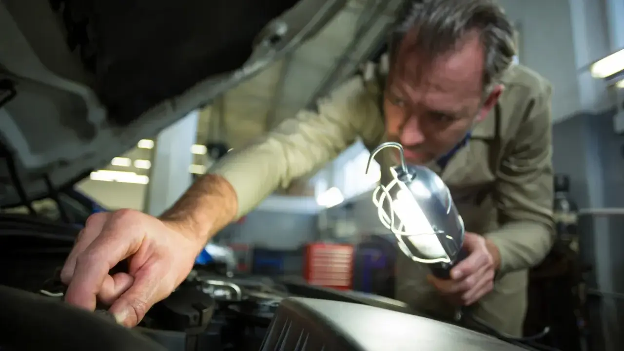Mechanik sprawdza bezpieczniki w Grande Punto, używając lampy inspekcyjnej.