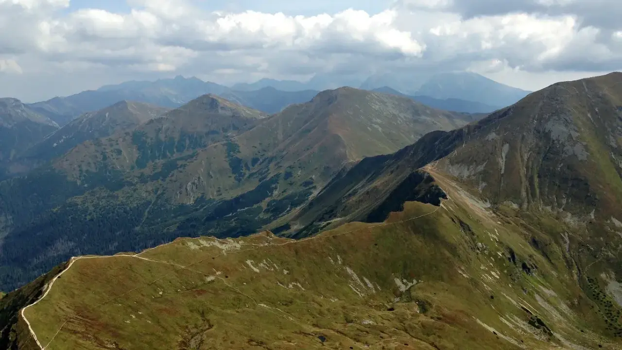 Widok na pasmo górskie, gdzie w Tatry prowadzi wydeptana ścieżka. Chmury na niebie.