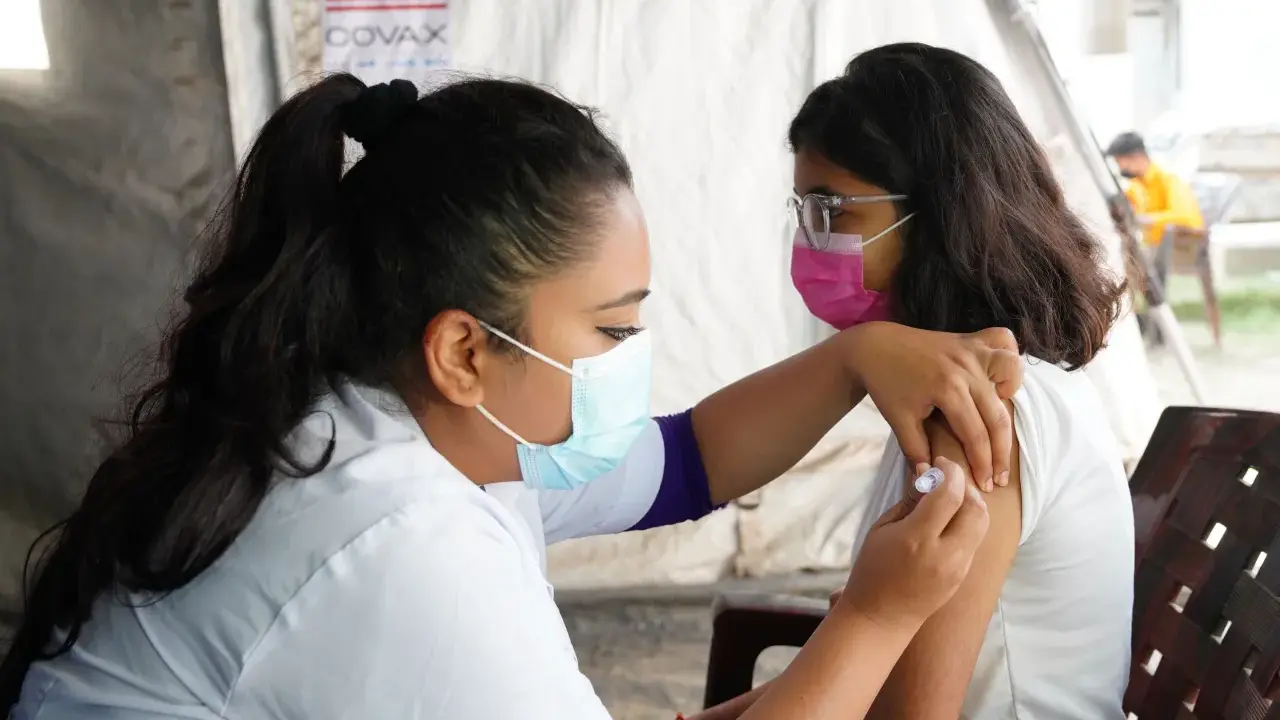 En sjuksköterska ger en vaccination i Nepal. Bakom syns en banderoll med texten COVAX och en amerikansk flagga.
