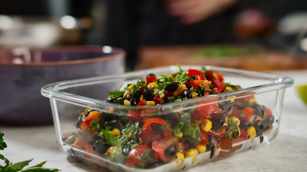 Frischer schwarze bohnen salat mit Mais, Tomaten und Kräutern in einer Glasbox.