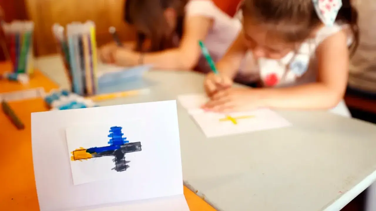 Dzieci rysują krzyże, ucząc się o religii w szkole. Na pierwszym planie symbol wiary.