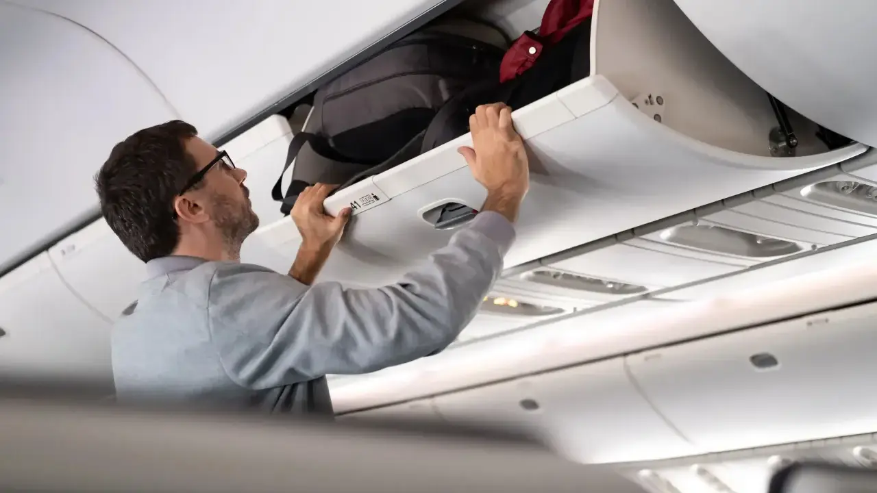 Man stänger bagagehyllan med handbagage ombord på ett flygplan från Austrian Airlines.