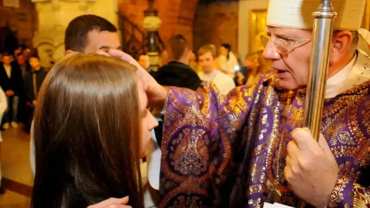 Biskup namaszcza czoło dziewczyny podczas bierzmowania. Czy bierzmowanie jest obowiązkowe? To ważny sakrament.