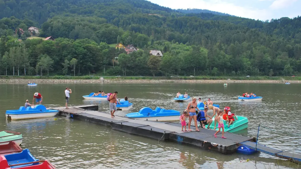 Wakacyjny dzień na Jeziorze Żywieckim. Ludzie pływają na rowerach wodnych, czując się jak na karaibskiej plaży.