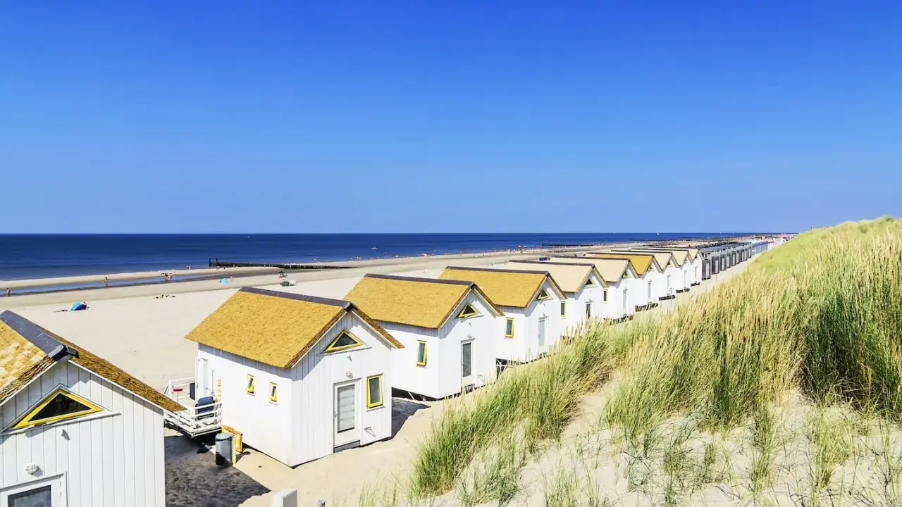 Reihen von weißen Strandhäusern mit gelben Dächern am **Holland Strand** unter blauem Himmel.