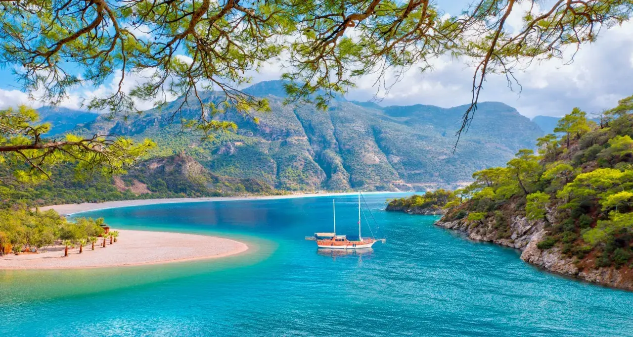 Malownicze widoki na turcja oludeniz: turkusowa woda, piaszczysta plaża i góry. Statek kołysze się na falach.