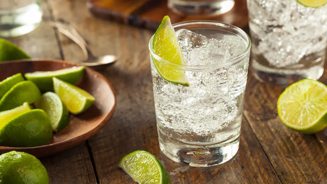 Erfrischender Gin und Bitter Lemon mit Eis und Limettenspalten auf rustikalem Holztisch.