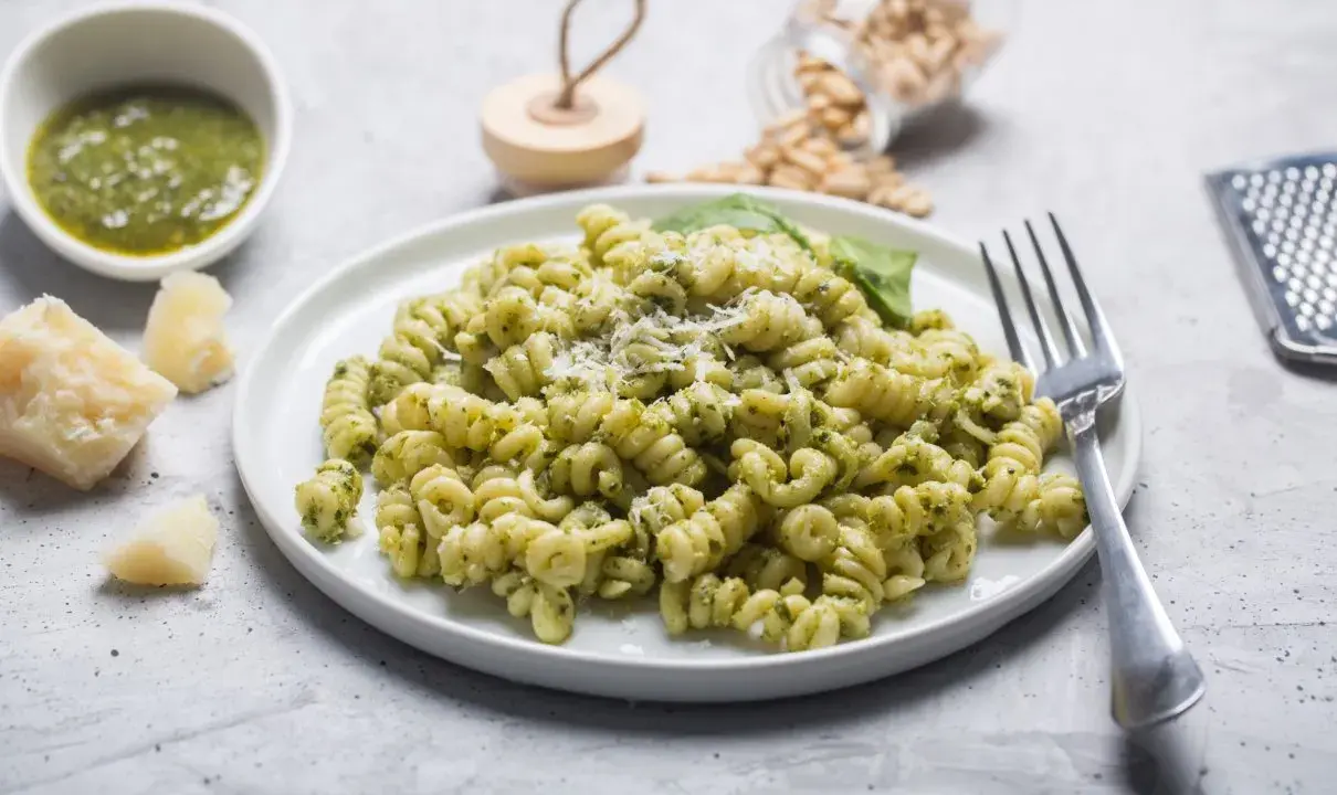 Pyszny makaron z pesto, posypany parmezanem, z dodatkiem świeżej bazylii i orzeszków piniowych.