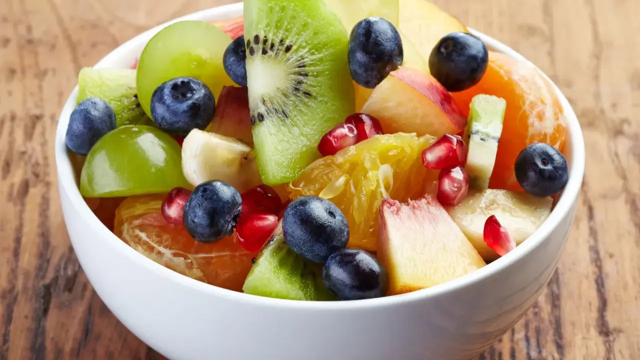 Kolorowa sałatka owocowa zimowa: kiwi, pomarańcza, winogrona, borówki, granat i brzoskwinia w białej misce.