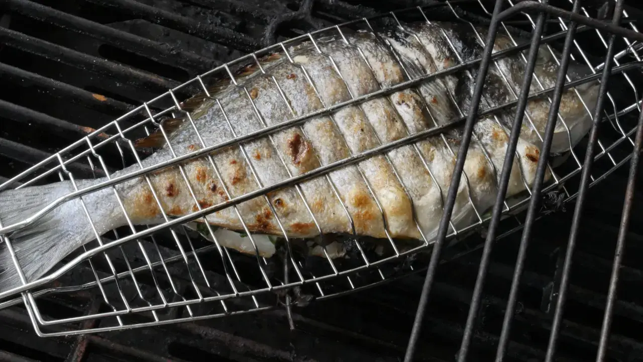 Ein ganzer Fisch wird in einem Grillkorb gegrillt. Die Haut ist goldbraun und leicht gebräunt.