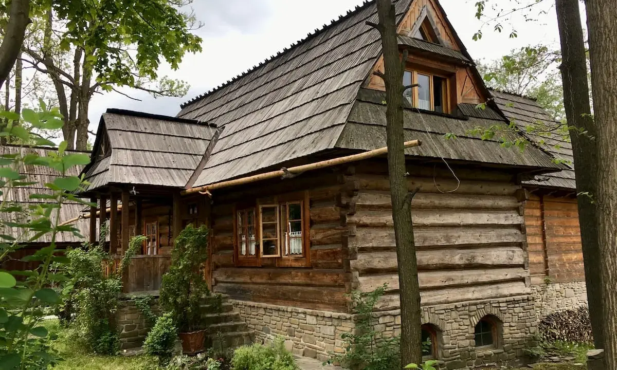 Drewniana chata z kamiennym fundamentem, kryta gontem, otoczona zielenią. Ulica Kościeliska w Zakopanem zachwyca tradycyjną architekturą.