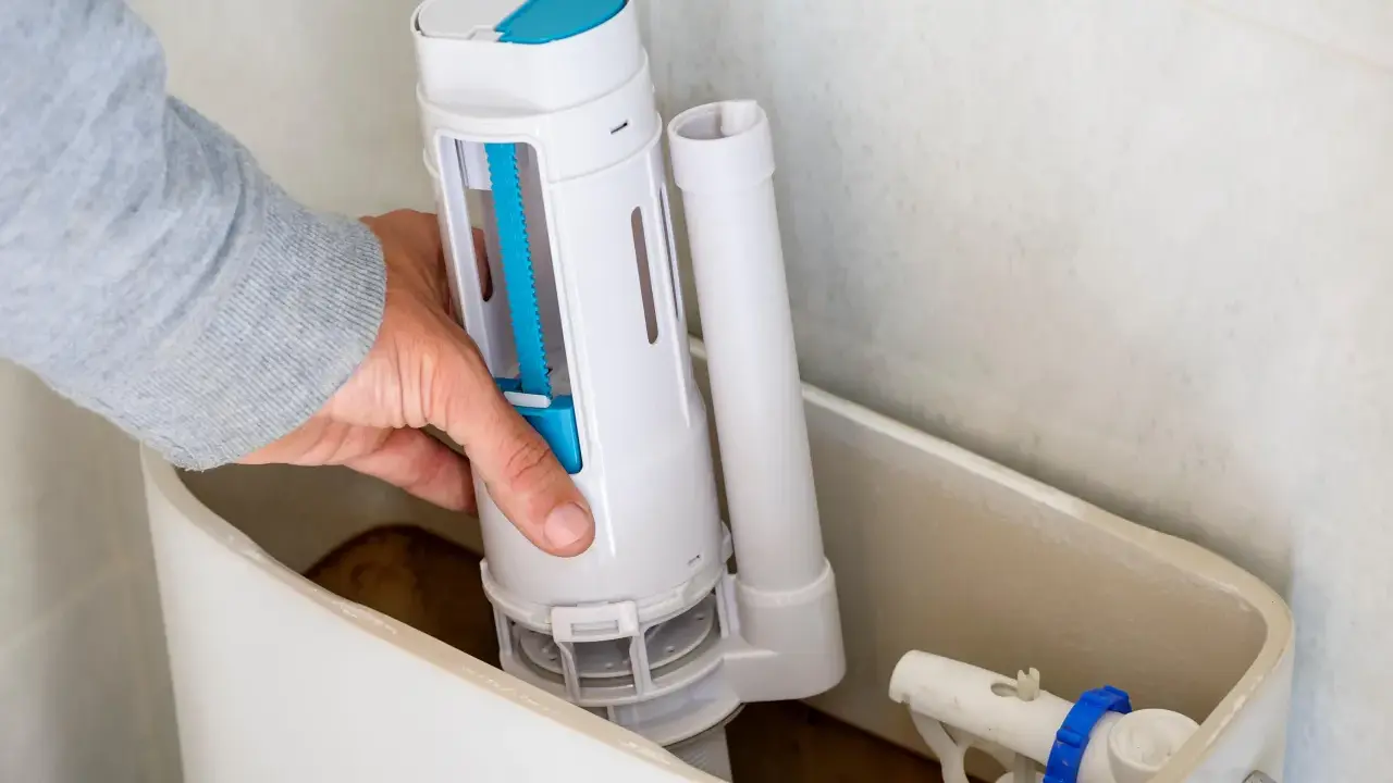 Mano instalando el mecanismo de descarga, una de las partes de una cisterna de baño. Se ve el flotador y la tubería de llenado.