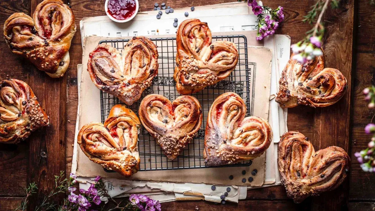 Herzförmige Hefeteilchen mit Marmelade und Nüssen, liebevoll arrangiert auf alten Notenblättern.