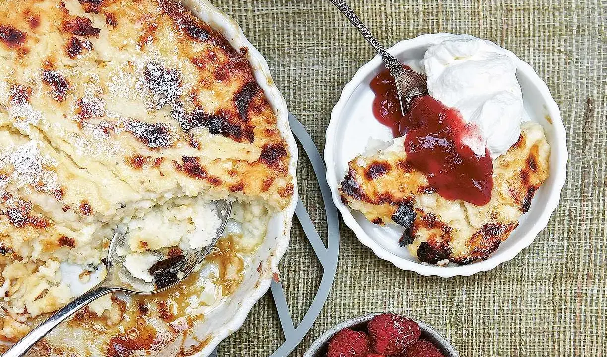En gyllene falsk ostkaka med krispiga kanter, serverad med vispad grädde, sylt och färska hallon.