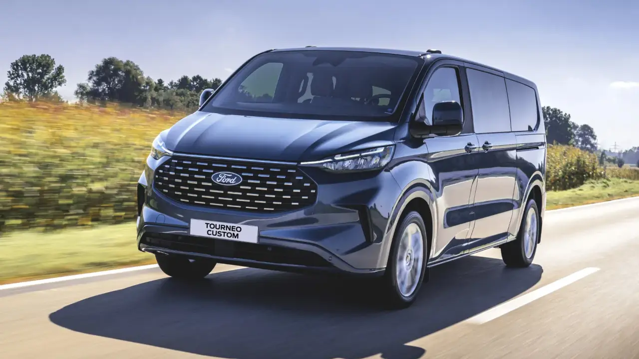 Ciemnoniebieski ford 7 osobowy Tourneo Custom pędzi po drodze wśród pól.