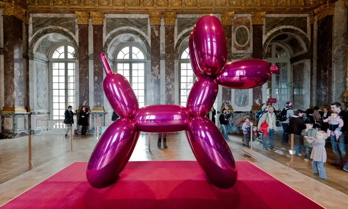 Jeff Coons' glänzender Ballonhund in Pink, ausgestellt in einem prunkvollen Saal mit Besuchern.