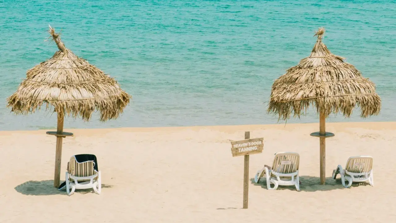 Idealna pogoda Tunezja wrzesień: dwa słomiane parasole i leżaki na piaszczystej plaży, turkusowe morze w tle.