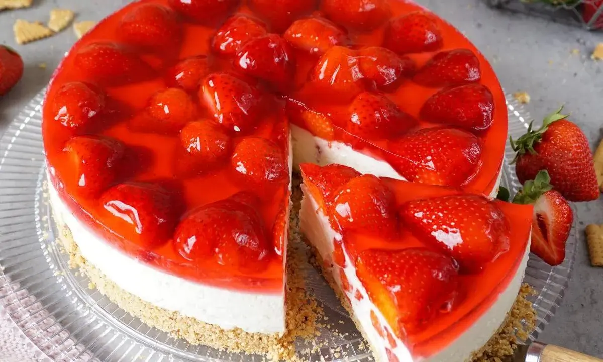 Ein saftiger erdbeerkuchen ohne backen mit frischen Erdbeeren und rotem Tortenguss. Ein Stück ist bereits angeschnitten.