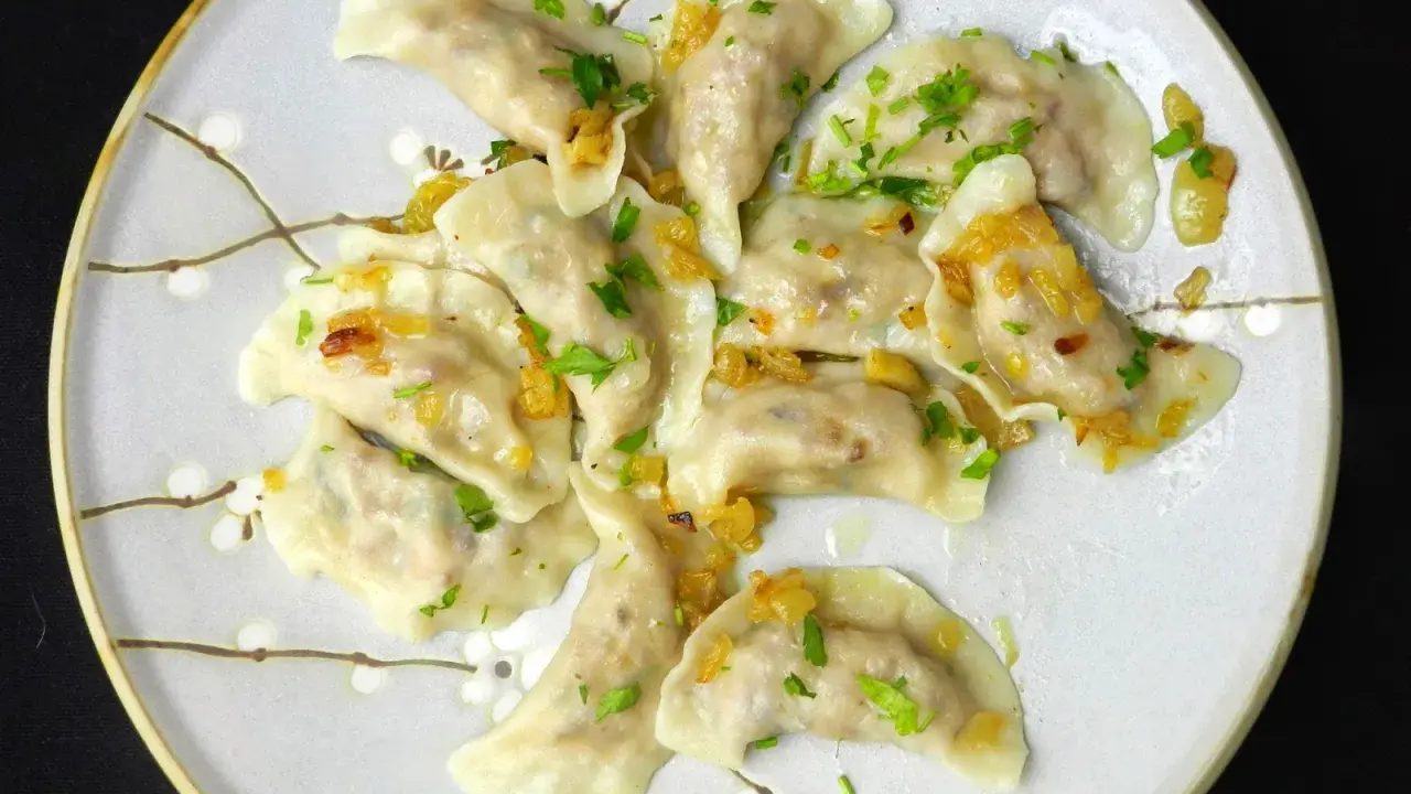 Pyszne pierogi z kaszą gryczaną, okraszone skwarkami i posypane natką pietruszki, na talerzu z delikatnym wzorem kwiatowym.