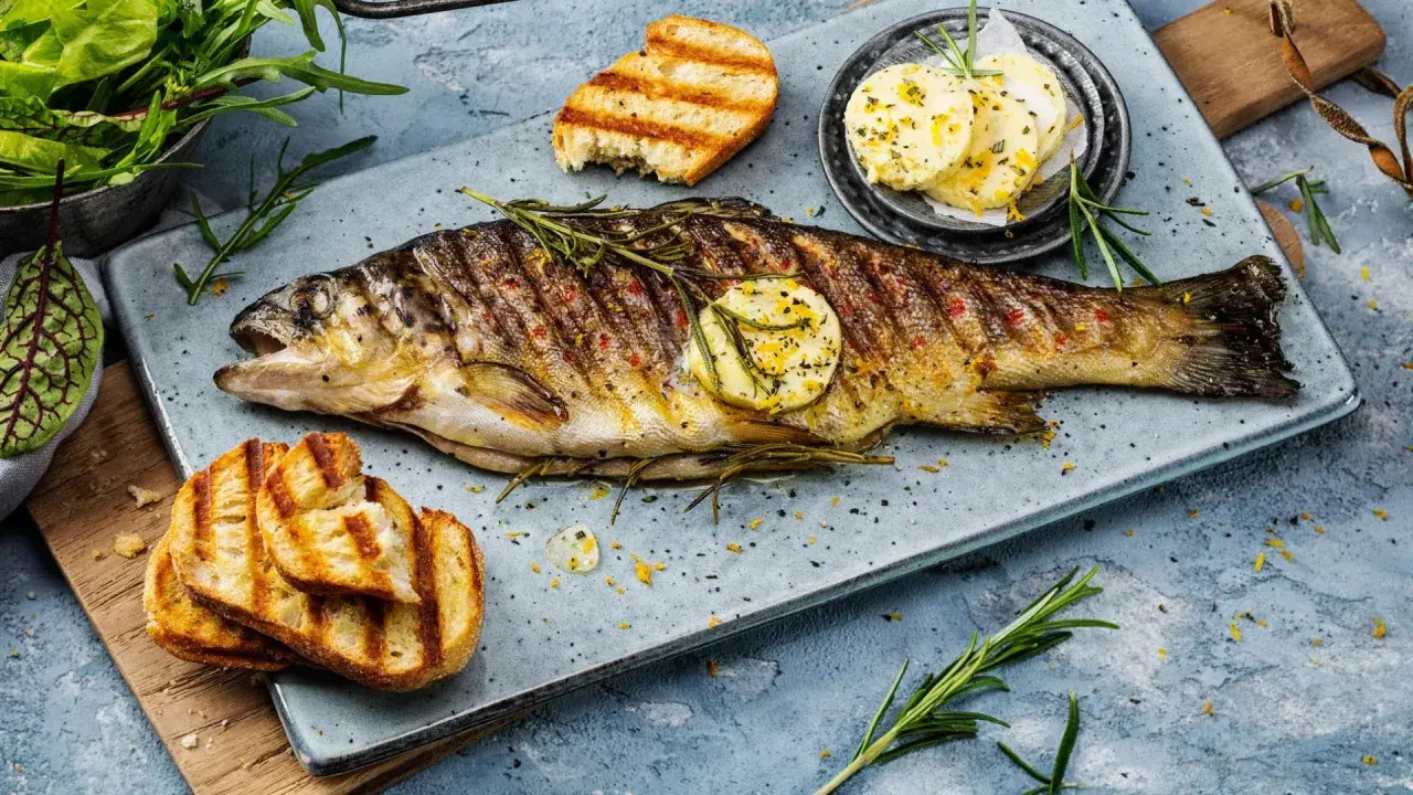 Perfekt gegrillte Forelle mit Kräutern, Zitronenscheibe und geröstetem Brot. Ein Genuss für jeden Fischliebhaber.