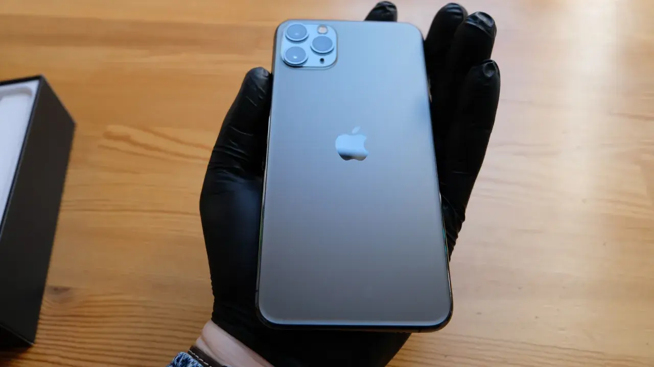 Ręka w czarnej rękawiczce trzyma elegancki iPhone 11 czarny. Obok leży czarne pudełko.