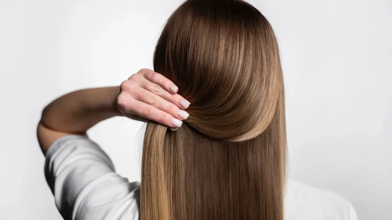 Capelli lisci e setosi, senza crespo, grazie a una routine efficace. La mano accarezza la chioma lucente.