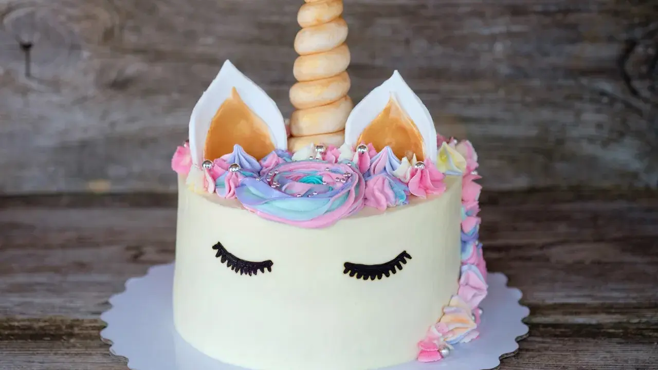 Ein magischer einhorn kuchen mit pastellfarbener Glasur, einem gedrehten Horn und süßen Wimpern.
