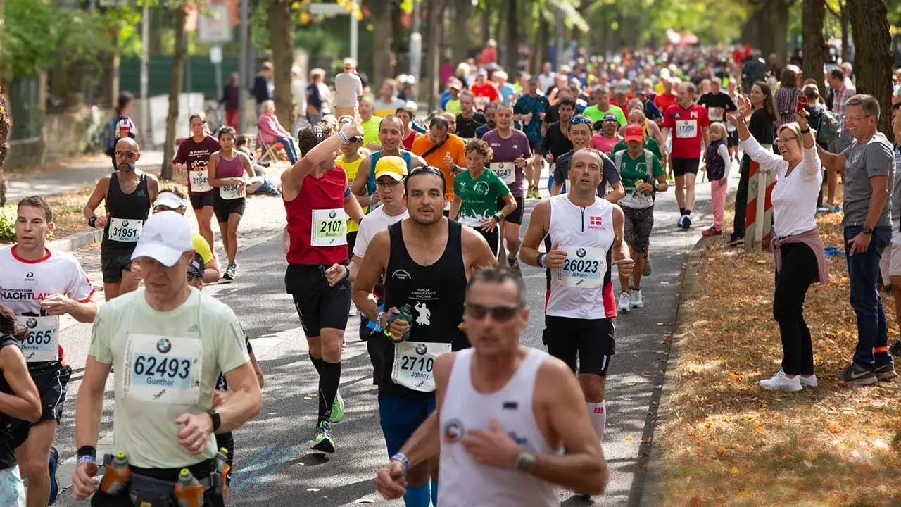 Läufer im Pulk auf einer Straße, einige mit Startnummern, die auf einen Marathon unter 4 Stunden hindeuten.