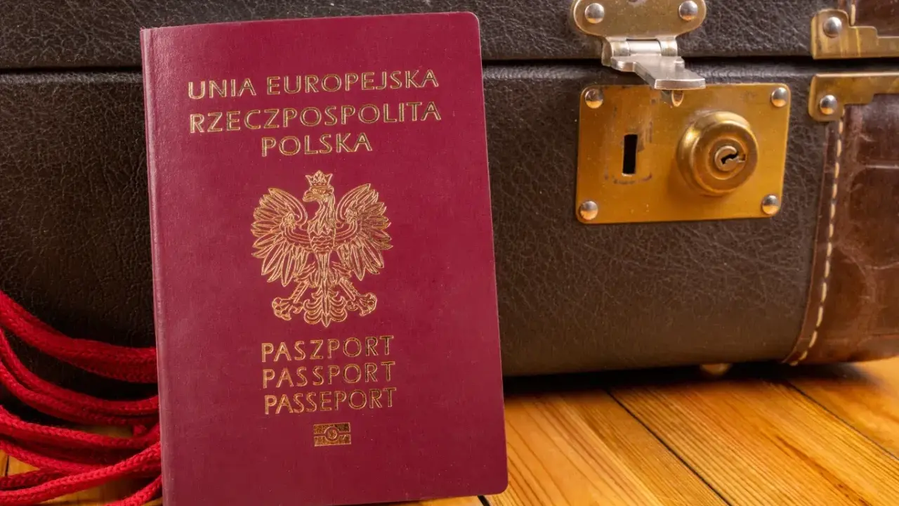 Polski paszport i brązowa walizka na drewnianym tle.