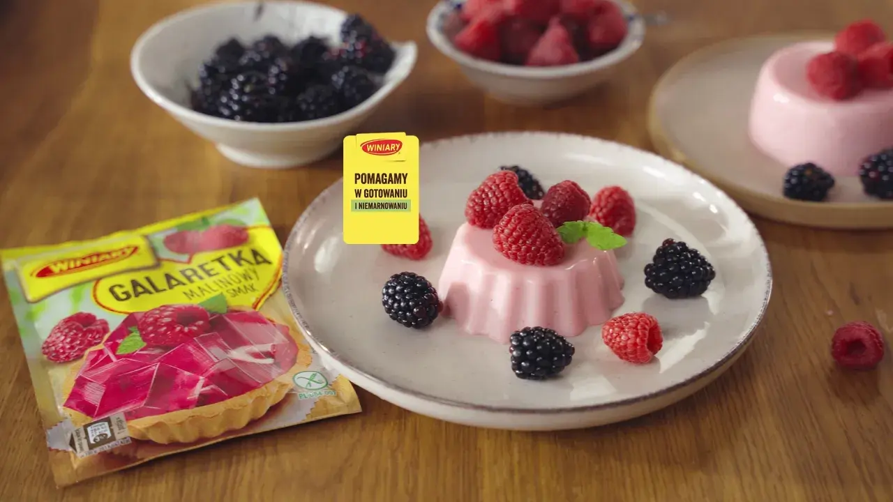Panna cotta z malinami i jeżynami, obok opakowanie galaretki malinowej.