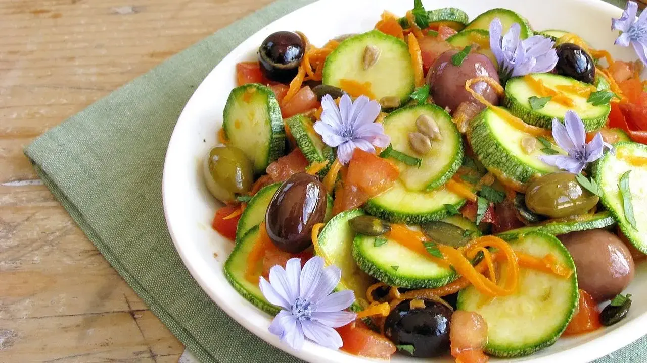 Insalata di zucchine fresca con pomodori, olive, carote e fiori di cicoria, un piatto colorato e leggero.