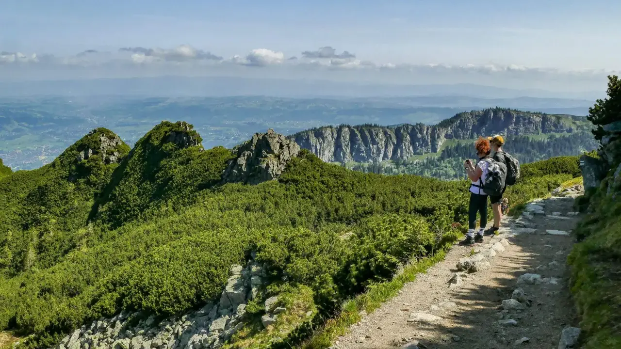 Dwie osoby z plecakami podziwiają widok na Tatry. Szlak jest kamienisty, ale stanowi łatwe zejście z Kasprowego Wierchu.