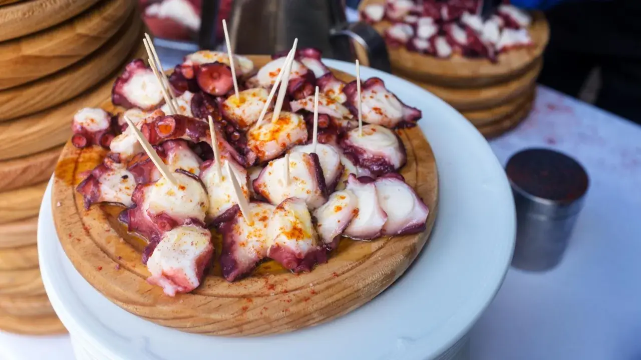 Pulpo a la gallega servido en tabla de madera, con palillos y espolvoreado con pimentón.