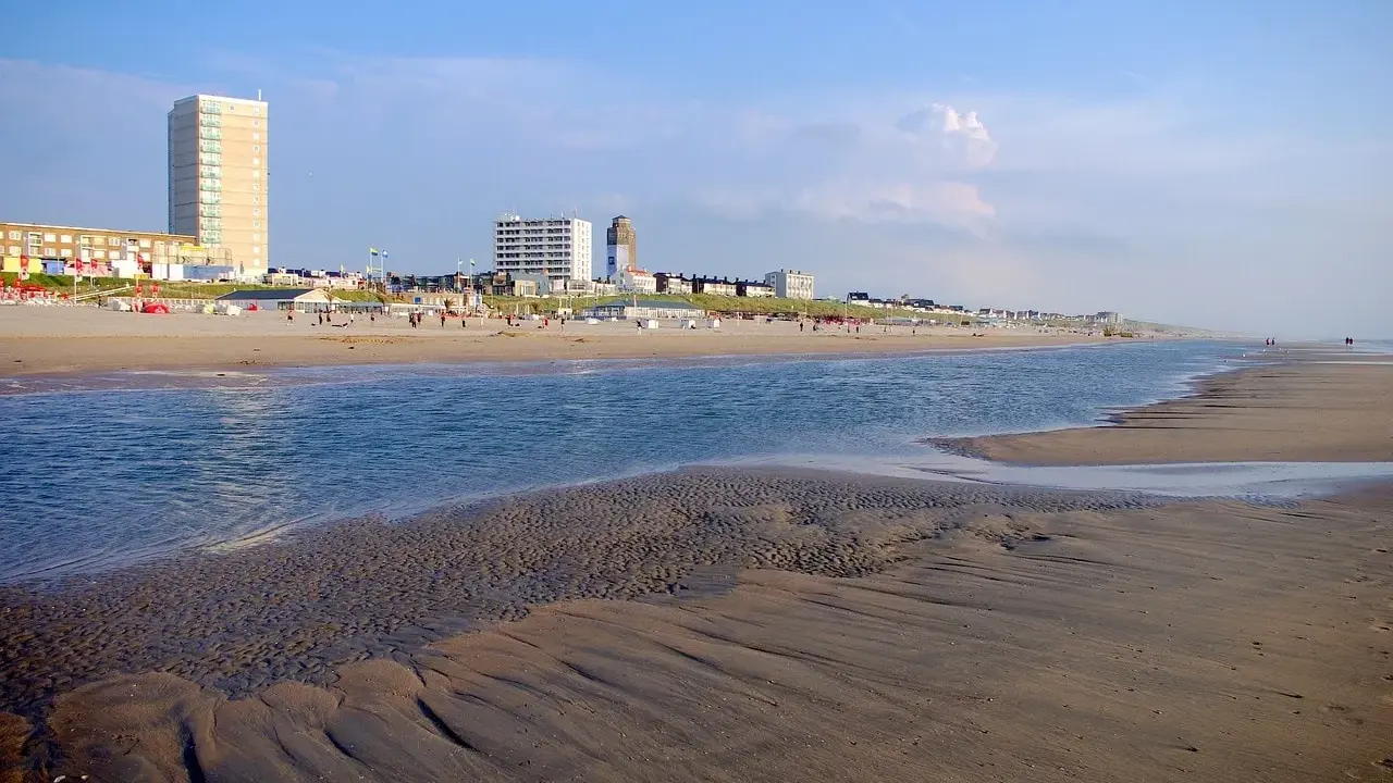 Piękny dzień nad morzem w Holandii. Piaszczysta plaża, spokojna woda i nowoczesne budynki w tle tworzą malowniczy krajobraz.