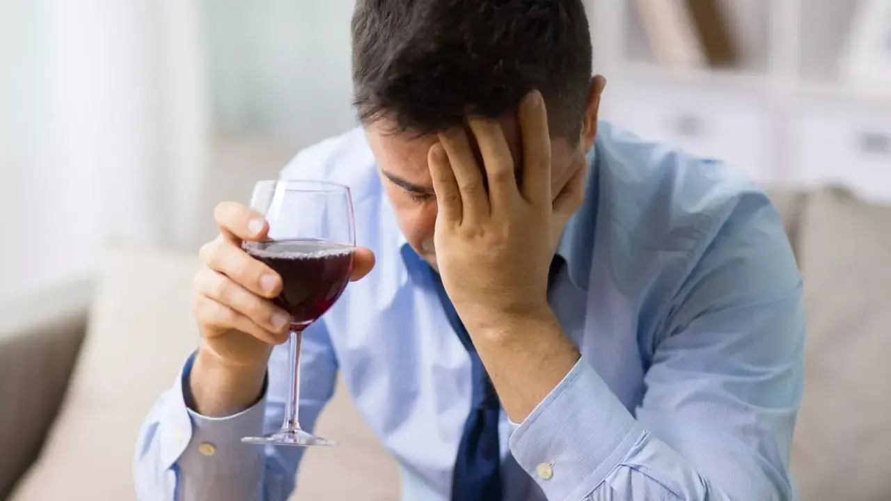 Hombre con copa de vino tinto, con la mano en la frente, buscando alivio en un vino sin histamina.