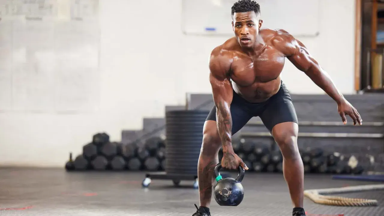 Ein Mann mit starkem Muskelaufbau hebt eine Kettlebell. Seine Anstrengung spiegelt die Ergebnisse von intensiven Trainingseinheiten wider, wie sie in Studien zum Muskelaufbau untersucht werden.