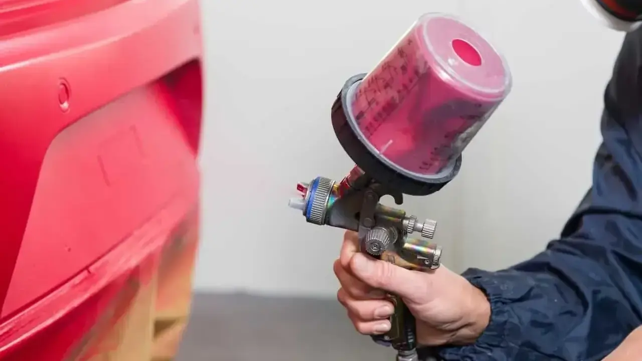 Profesjonalne malowanie zderzaka na czerwono. Pistolet lakierniczy z różową farbą w zbiorniku.