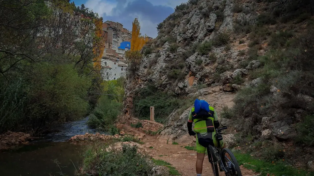 Ciclista en la ruta de las esculturas Bogarra, junto a un río y un pueblo en la ladera.