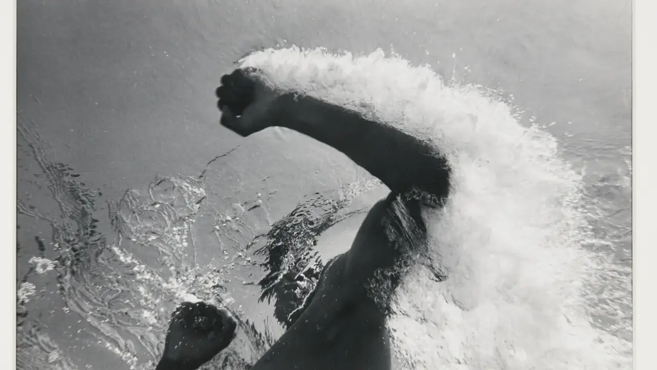 Underwater shot of a swimmer's arms and torso, creating a dramatic splash. The image captures the power and motion of a flip schulke.